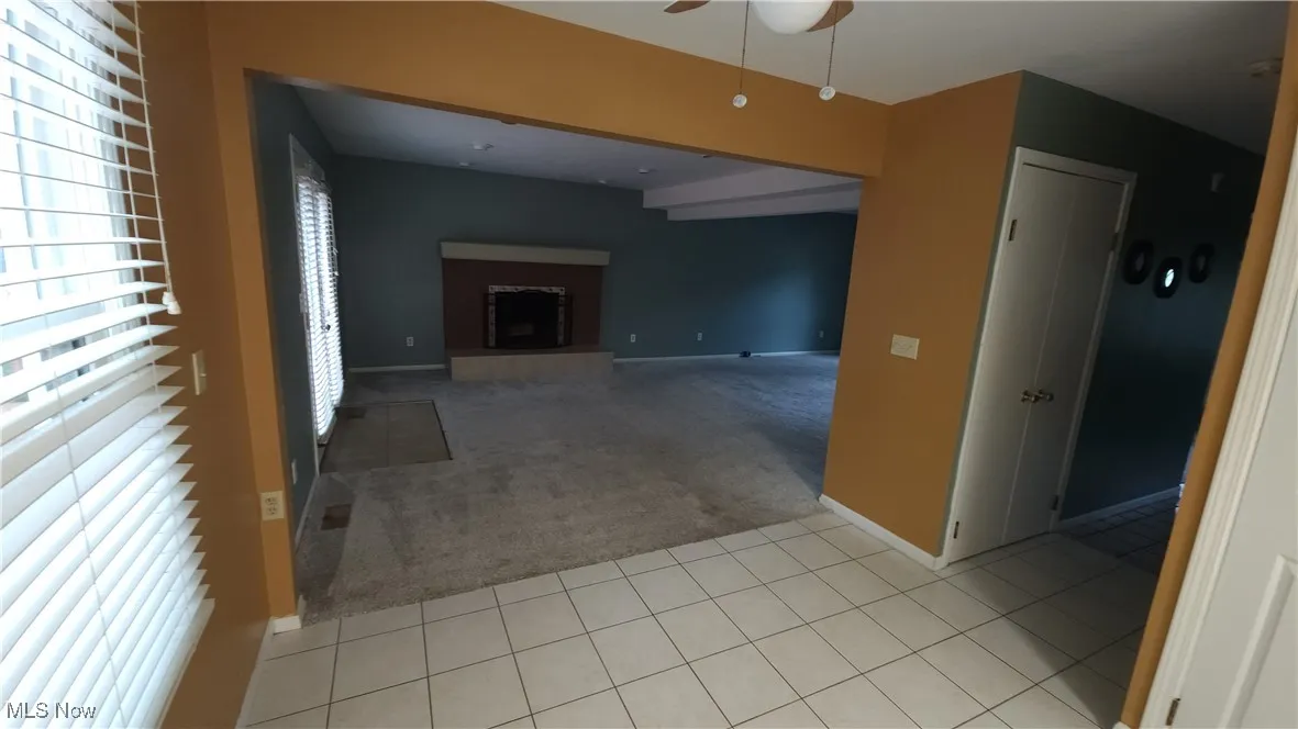 Unfurnished living room featuring light colored carpet, light tile patterned floors, a fireplace with raised hearth, and a ceiling fan
