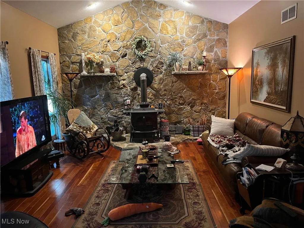 Living room featuring a wood stove, vaulted ceiling, and hardwood / wood-style flooring