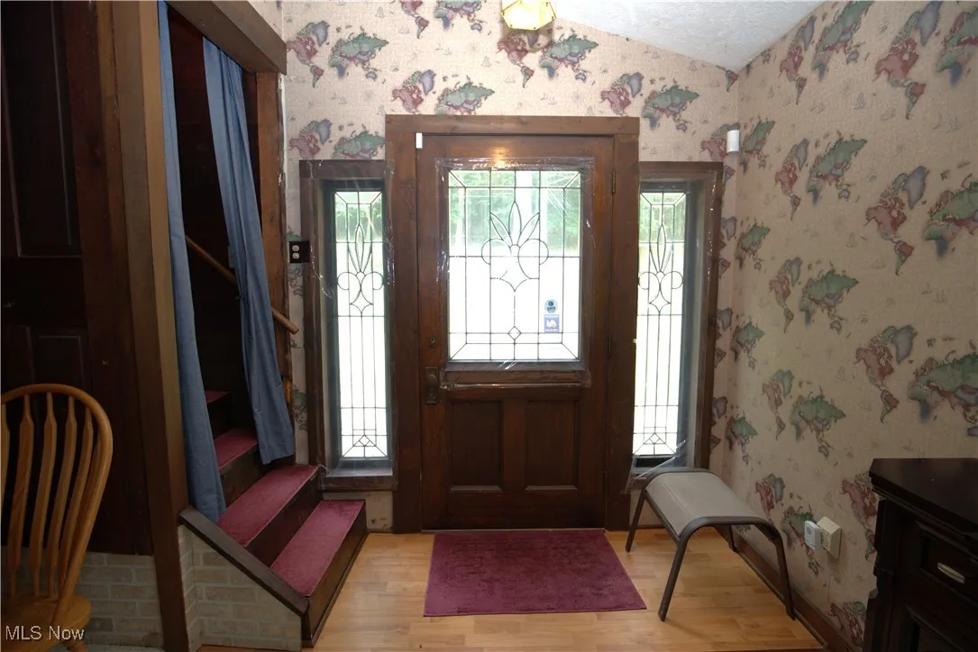 Entrance foyer with wallpapered walls, wood finished floors, vaulted ceiling, and plenty of natural light