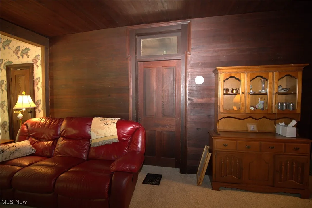 Living area with wood ceiling, light colored carpet, and wooden walls
