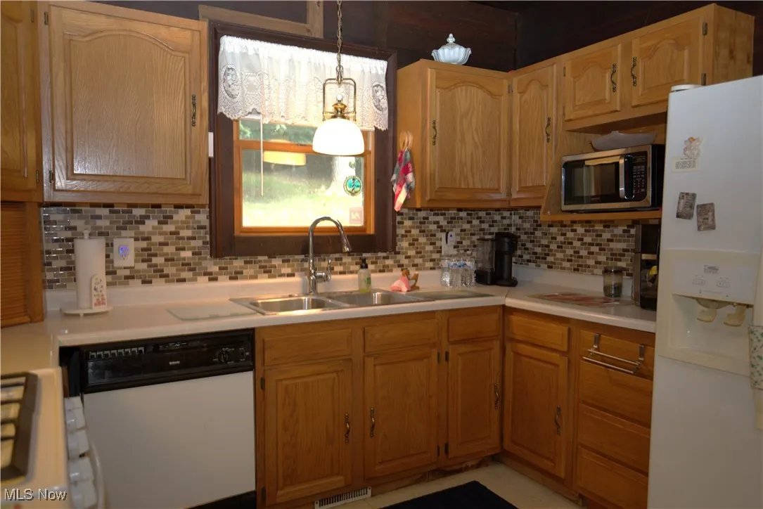 Kitchen featuring white appliances, light countertops, tasteful backsplash, brown cabinetry, and pendant lighting