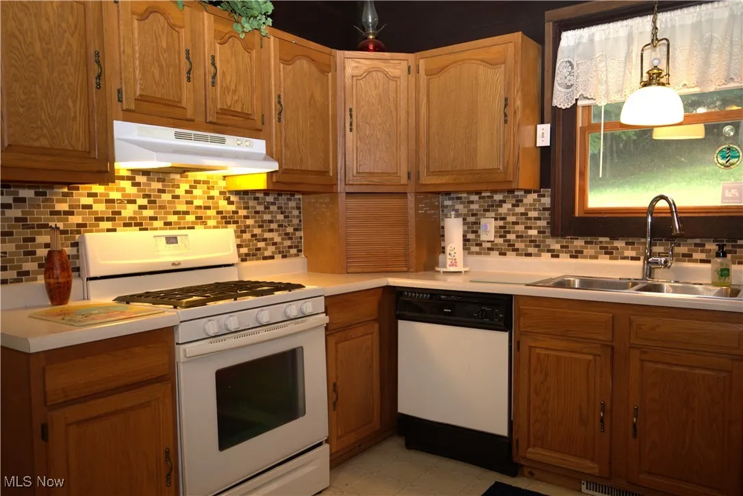 Kitchen featuring white appliances, tasteful backsplash, light countertops, under cabinet range hood, and brown cabinets