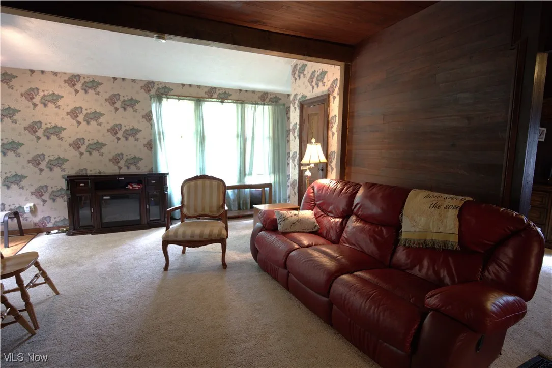 Carpeted living room featuring a wood ceiling with exposed beams, and wallpapered walls