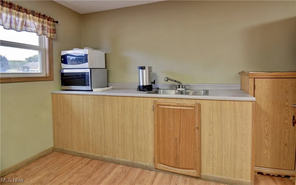 Kitchen with light countertops, light wood-style floors, stainless steel microwave, and white microwave