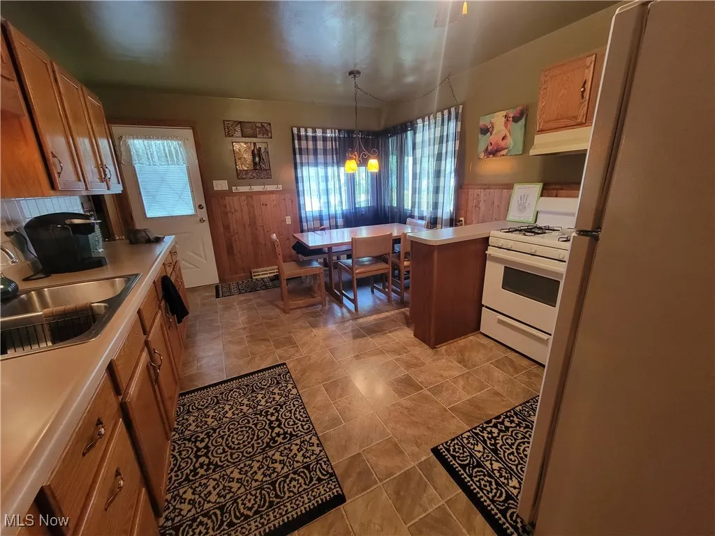 Kitchen with white appliances, wainscoting, hanging light fixtures, brown cabinets, and light countertops