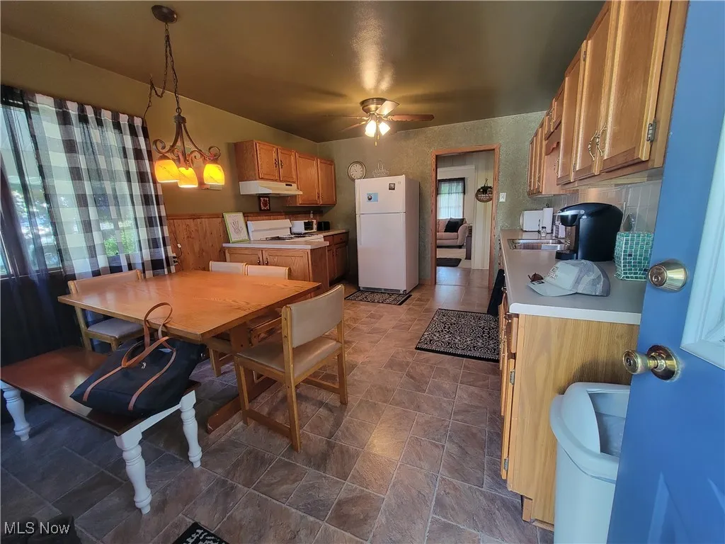 Kitchen featuring light countertops, freestanding refrigerator, brown cabinets, pendant lighting, and under cabinet range hood
