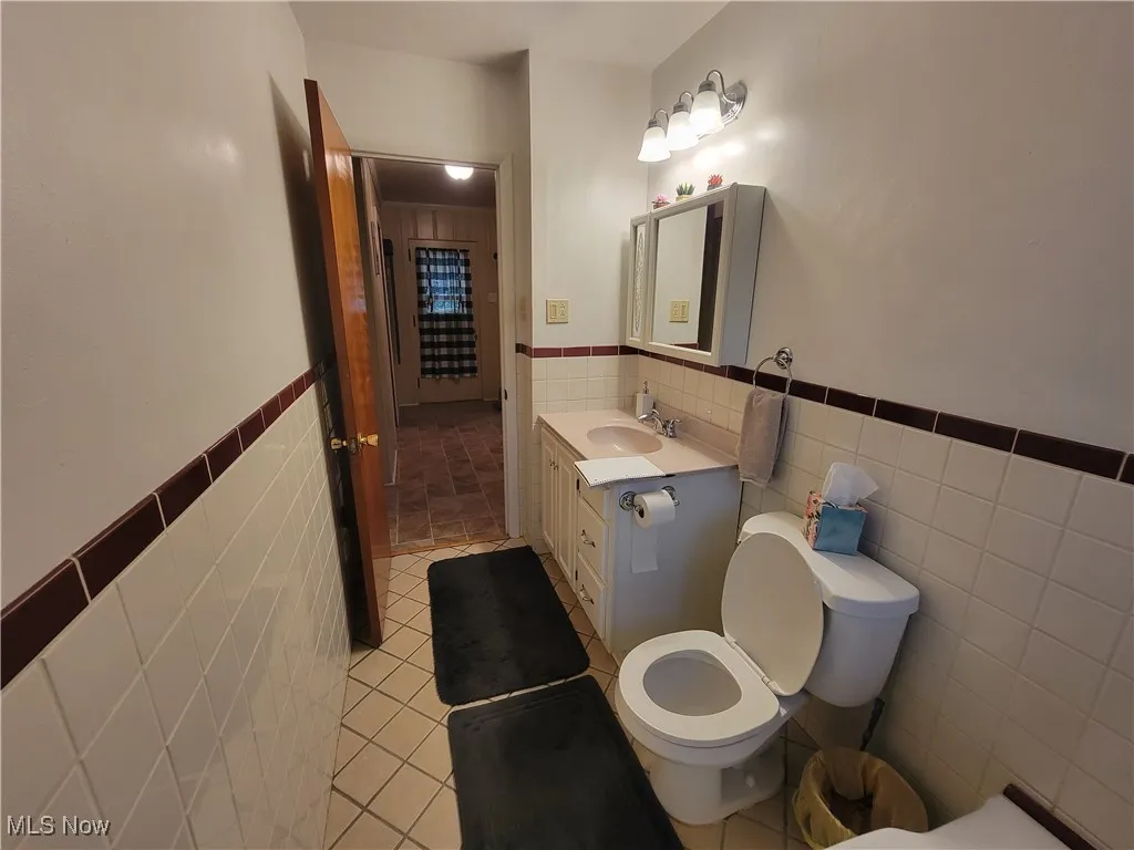 Bathroom featuring light tile patterned floors, tile walls, vanity, and wainscoting