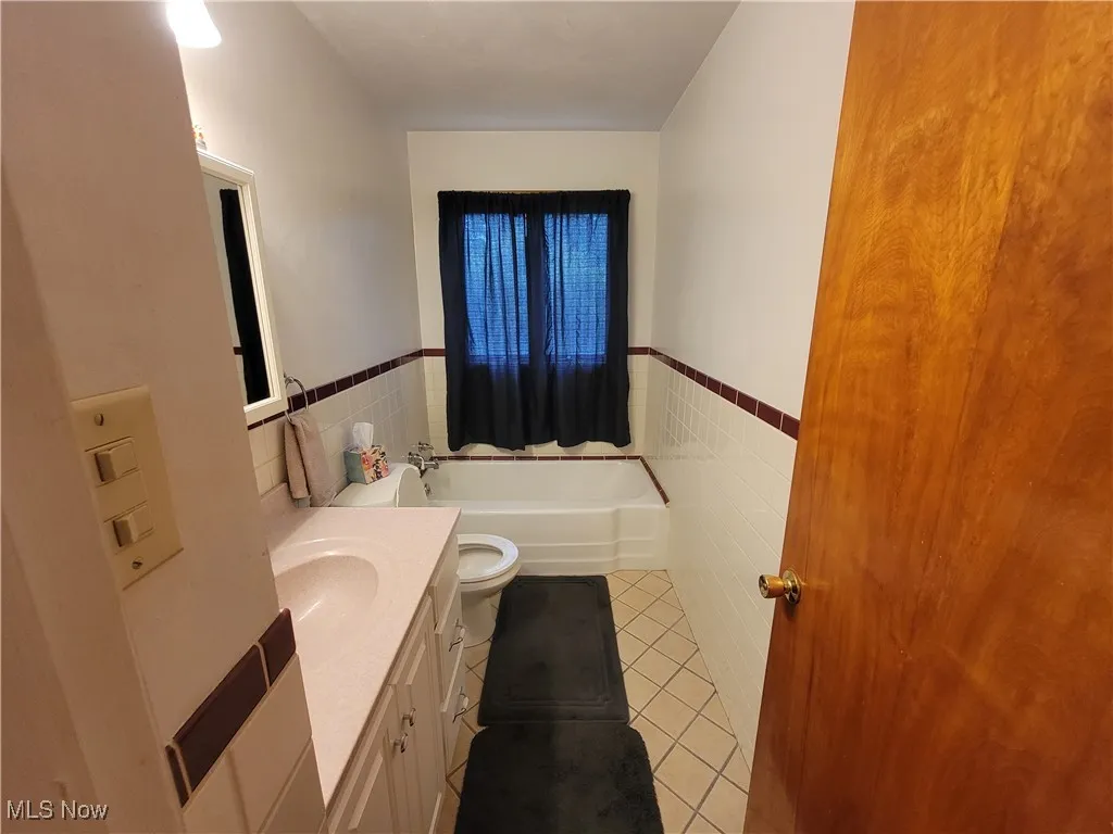 Full bath featuring tile walls, tile patterned flooring, vanity, a garden tub, and a wainscoted wall
