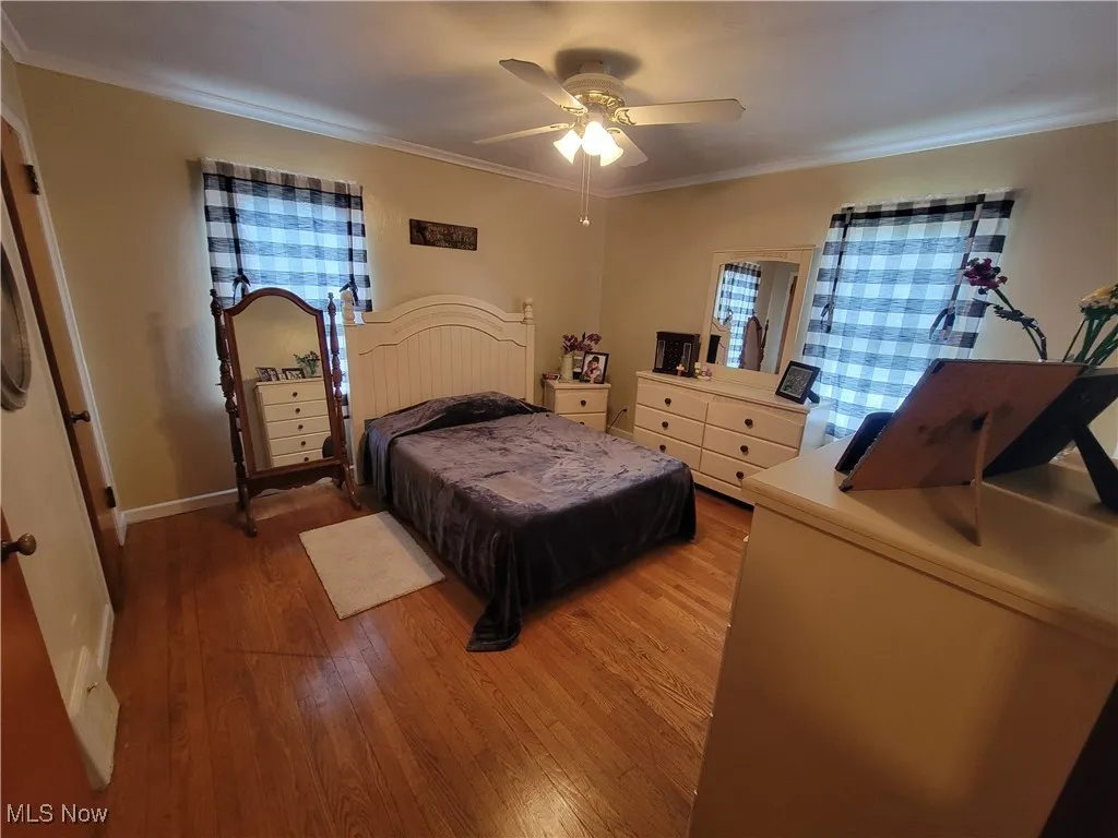 Bedroom featuring wood-type flooring, ornamental molding, and a ceiling fan