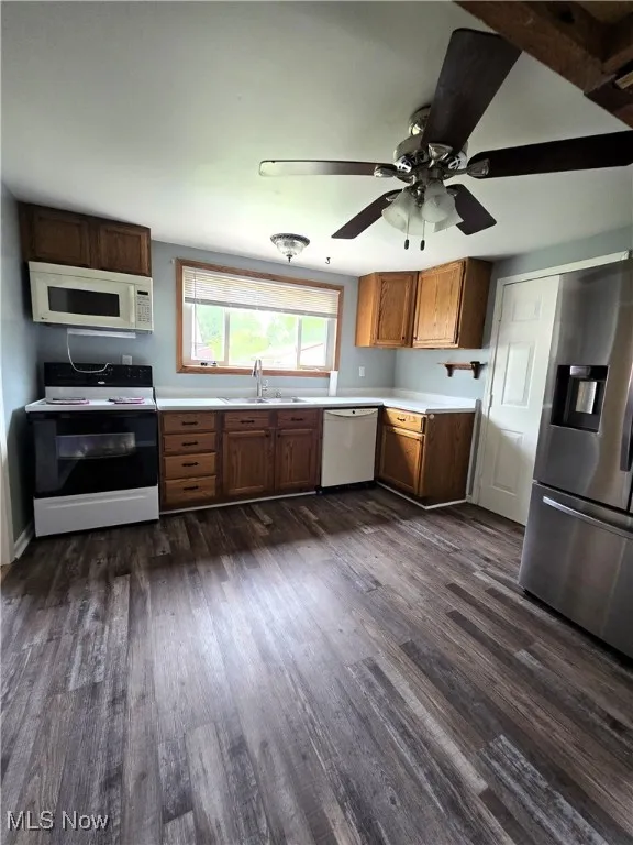 Kitchen featuring white appliances, light countertops, dark wood finished floors, ceiling fan, and brown cabinets