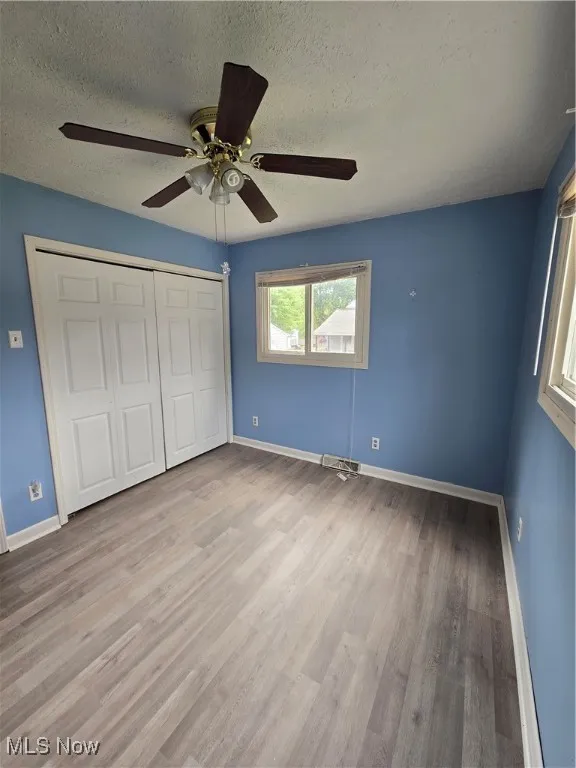 Unfurnished bedroom with a textured ceiling, a closet, a ceiling fan, and light wood-style floors