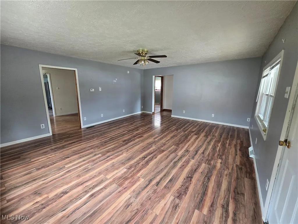 Unfurnished room featuring a textured ceiling, plenty of natural light, dark wood finished floors, and ceiling fan