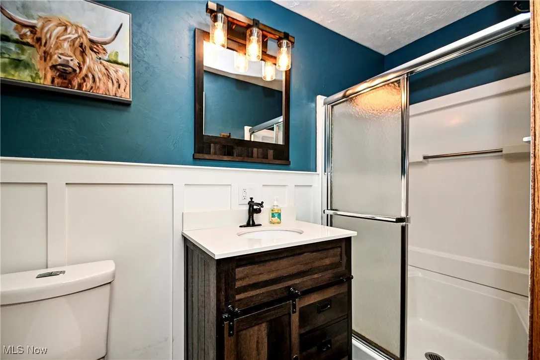 Full bathroom featuring a decorative wall, a stall shower, vanity, and wainscoting