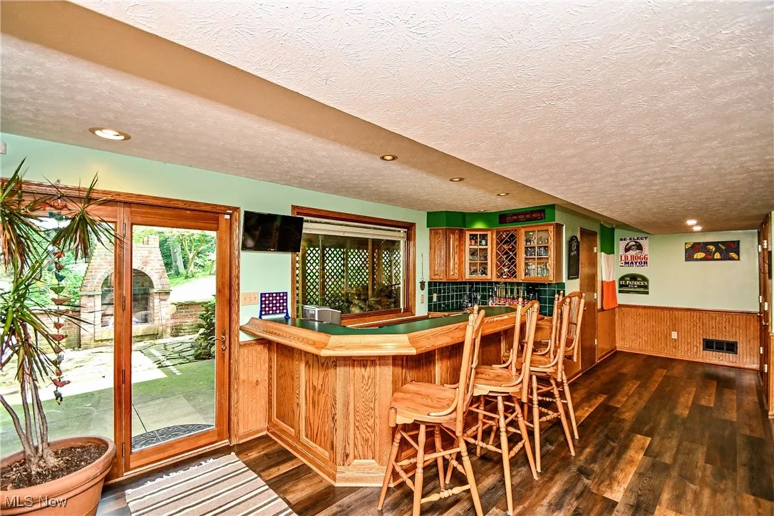 Bar in lower level basement featuring a textured ceiling, dark wood-style floors, wainscoting, recessed lighting, and wooden walls