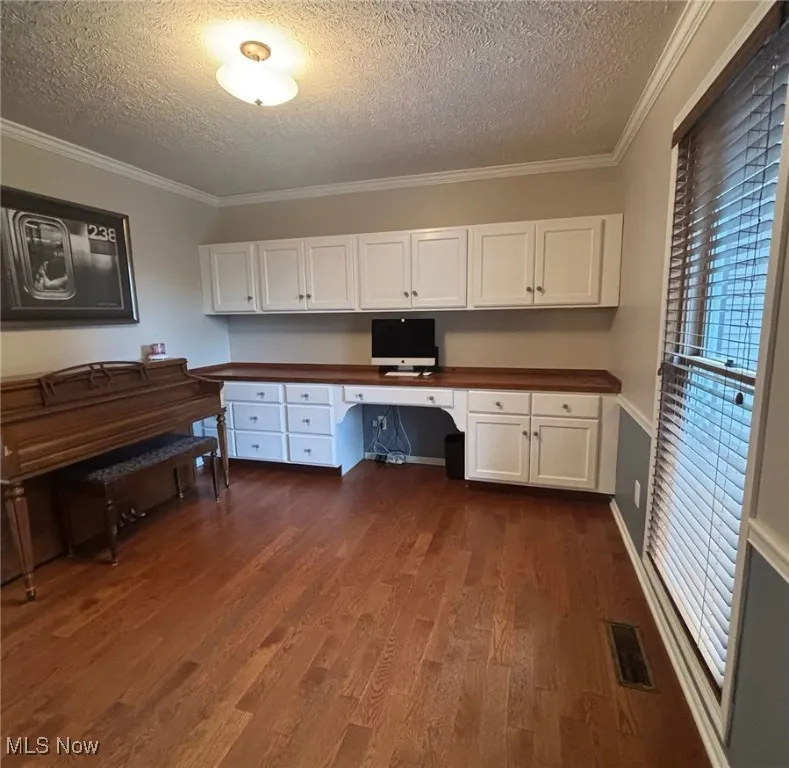Home office featuring built in desk, a textured ceiling, crown molding, and dark wood-style flooring