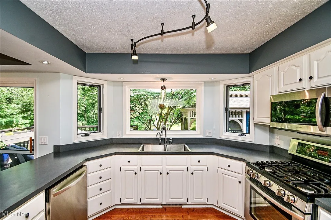 Kitchen with appliances with stainless steel finishes, dark countertops, a textured ceiling, and white cabinets