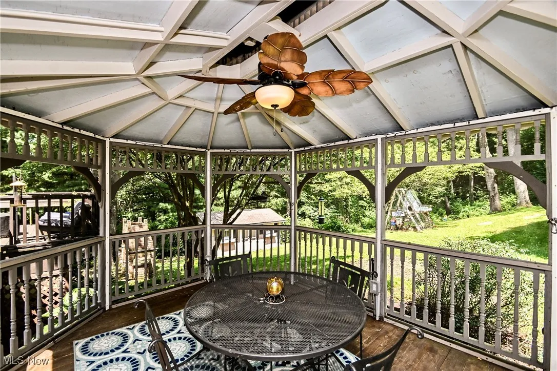 Wooden terrace with outdoor dining space, a ceiling fan, a lawn, and a gazebo