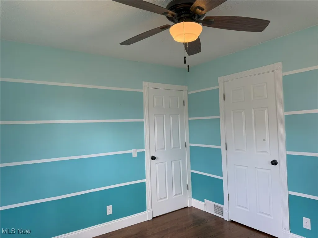 Unfurnished bedroom with dark wood-style floors and a ceiling fan