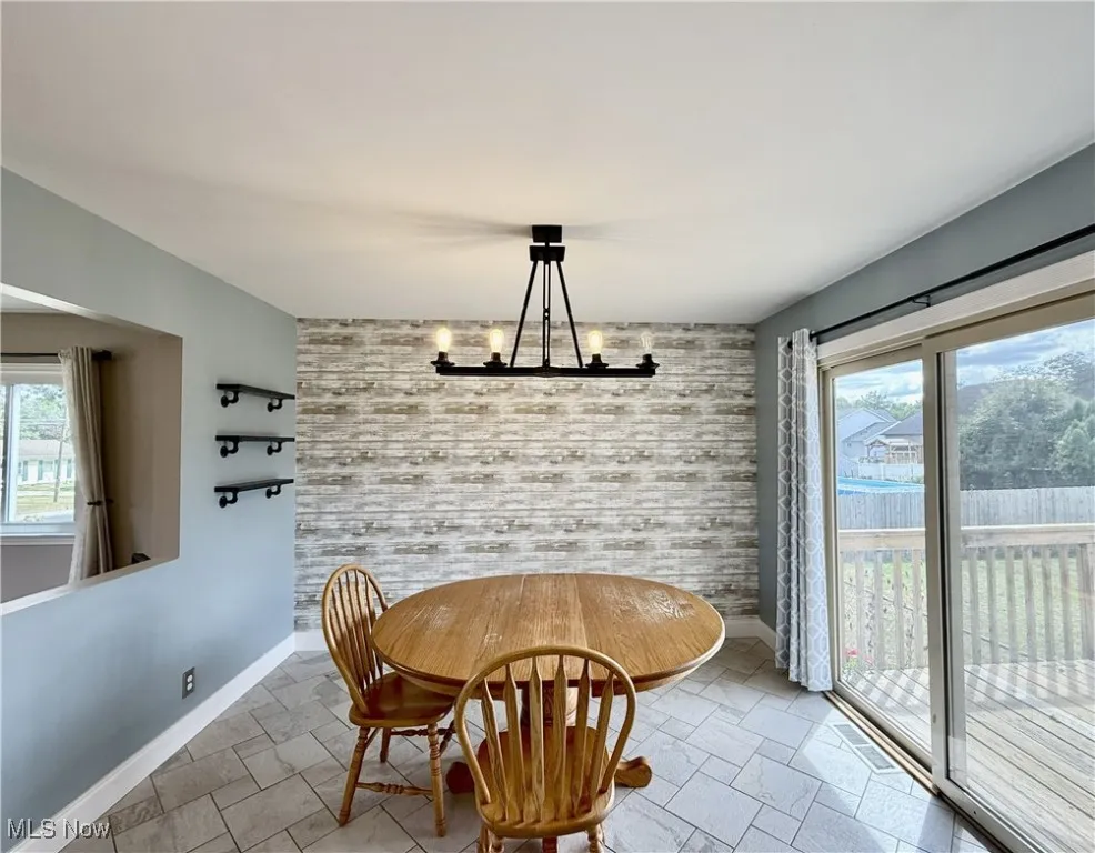 Dining area with an accent wall, a chandelier, and stone tile flooring