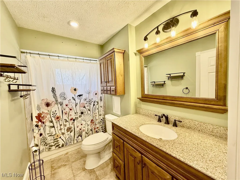 Bathroom featuring a textured ceiling, vanity, shower / bath combination with curtain, and light tile patterned floors