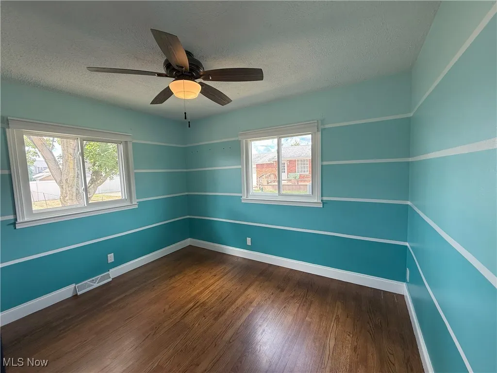 Unfurnished room with dark wood-style floors, a textured ceiling, and ceiling fan
