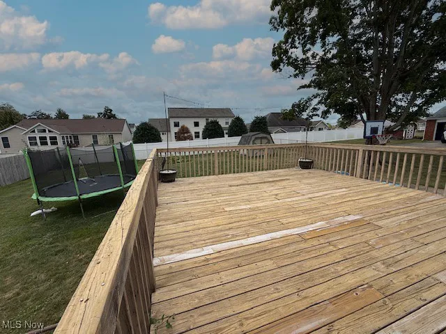 Wooden terrace with a trampoline, a residential view, and a fenced backyard