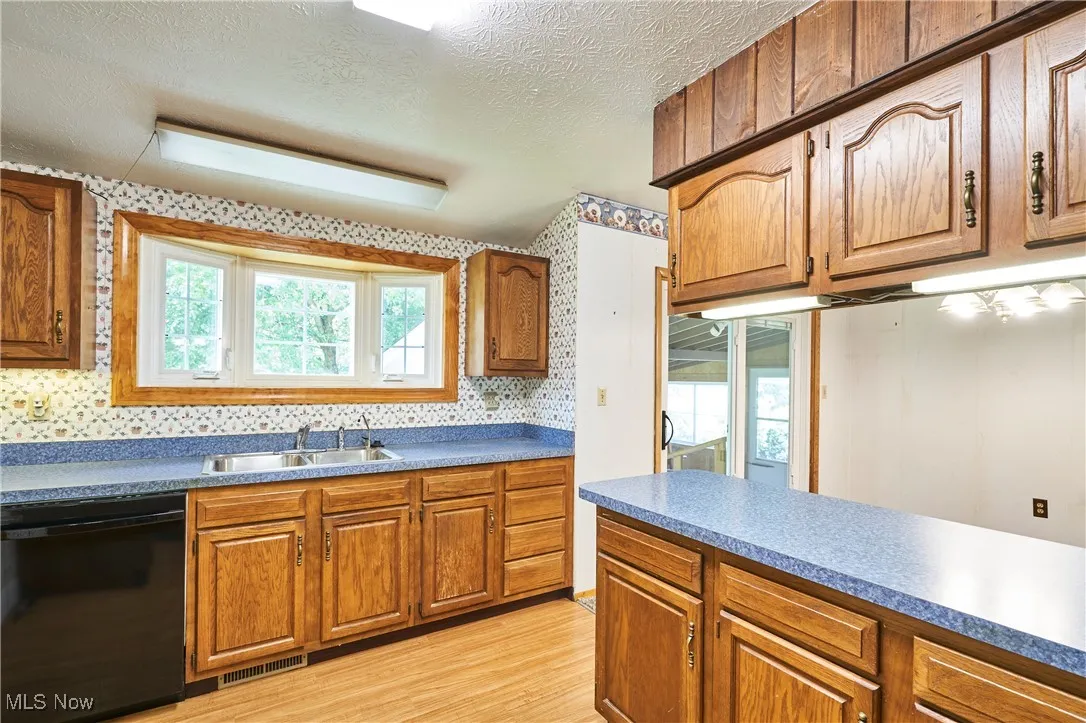 Kitchen featuring brown cabinets, dishwasher, a textured ceiling, light wood-style floors, and backsplash