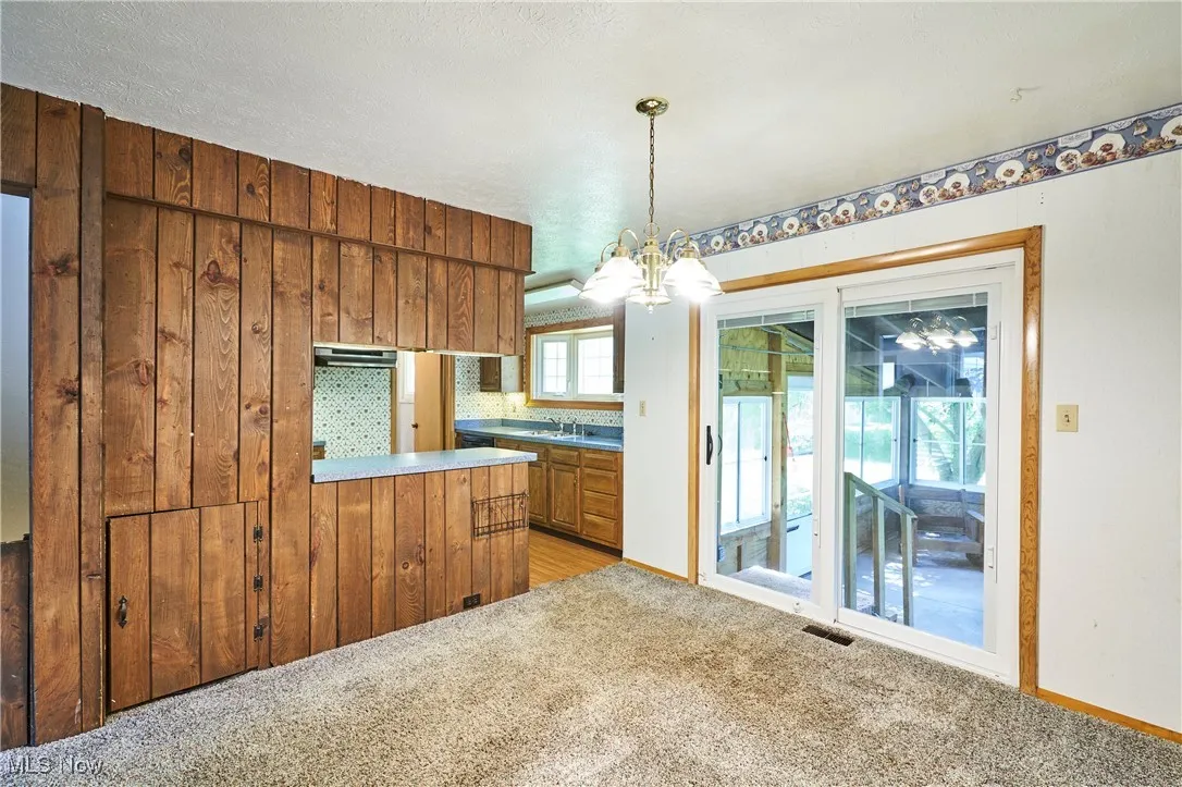 Kitchen featuring light carpet, hanging light fixtures, a chandelier, brown cabinets, and light countertops