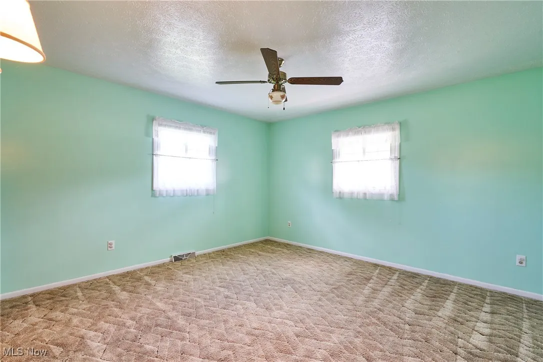 Carpeted empty room with a textured ceiling and ceiling fan
