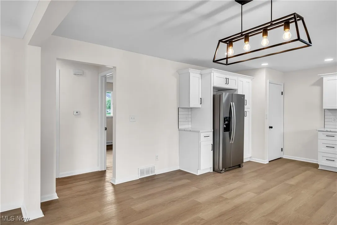Kitchen featuring stainless steel fridge with ice dispenser, white cabinets, decorative light fixtures, light wood-type flooring, and decorative backsplash
