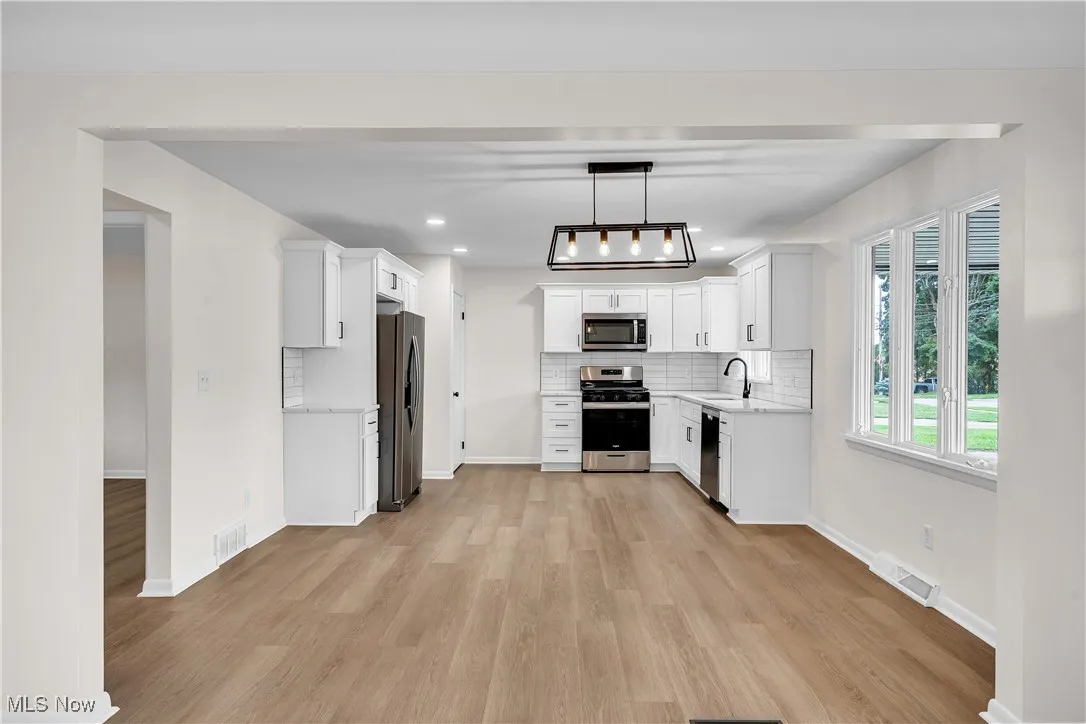 Kitchen with white cabinets, decorative backsplash, appliances with stainless steel finishes, light wood-style flooring, and pendant lighting