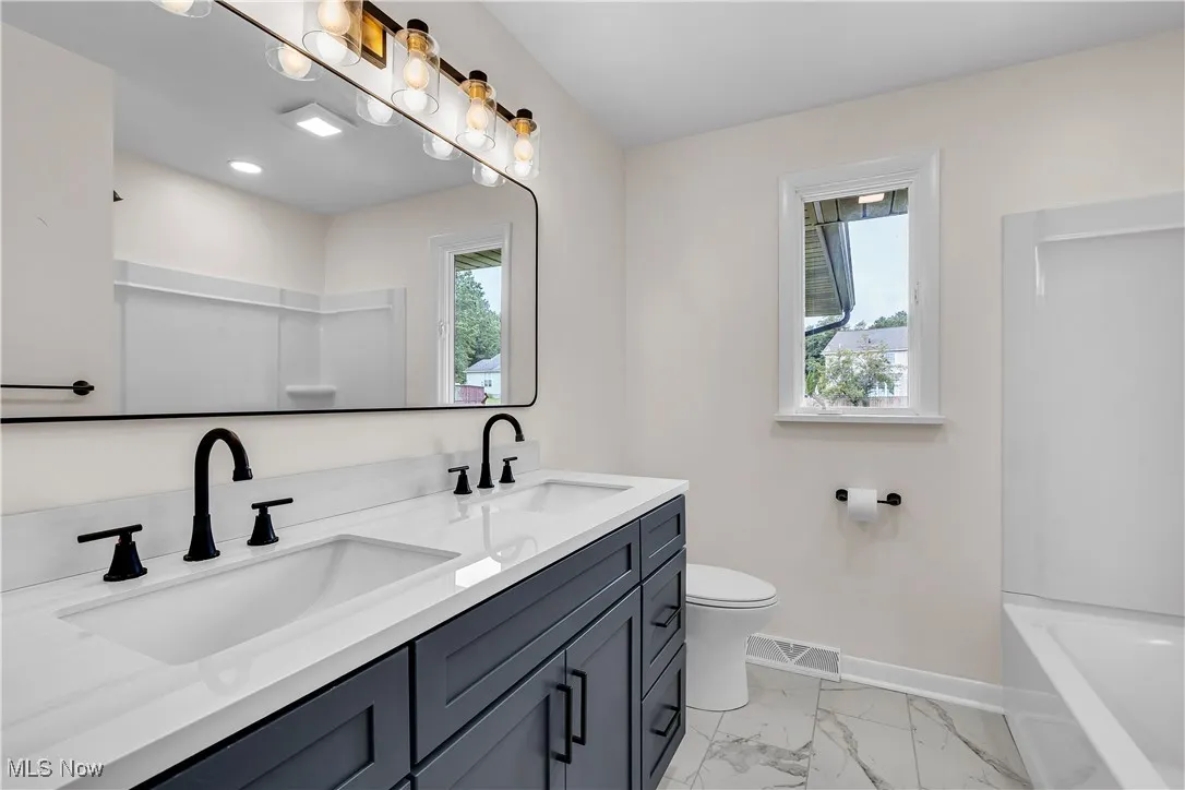 Bathroom with double vanity, light marble finish flooring, and shower / tub combination