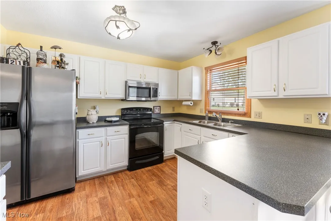Kitchen with appliances with stainless steel finishes, dark countertops, white cabinetry, and light wood-type flooring