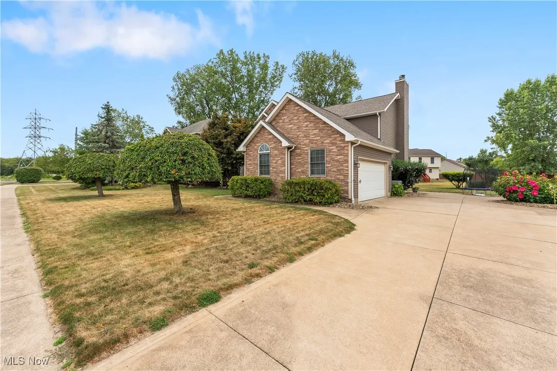 View of front facade featuring a chimney, brick siding, concrete driveway, a front yard, and a garage