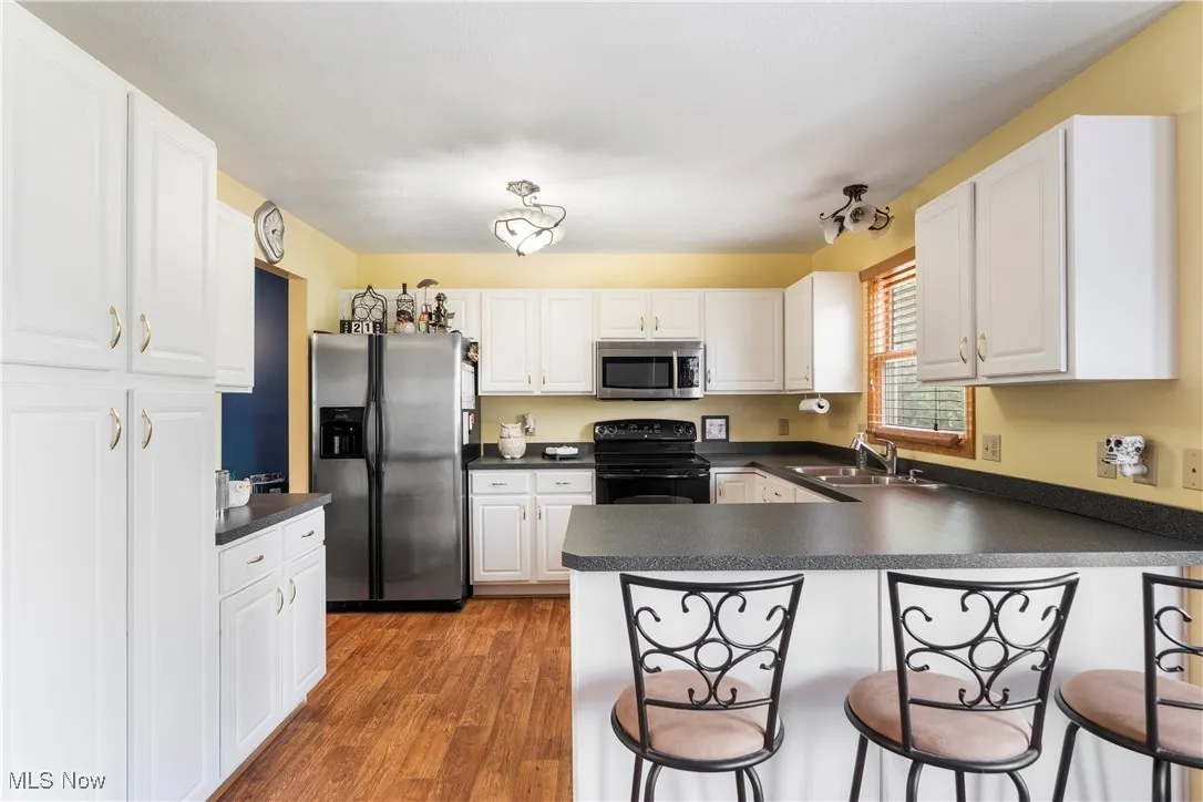 Kitchen with dark countertops, a peninsula, white cabinetry, appliances with stainless steel finishes, and a kitchen bar