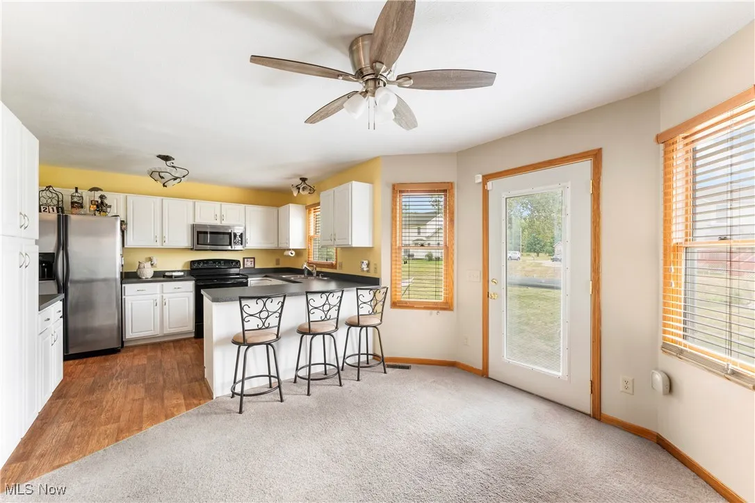 Kitchen featuring dark countertops, stainless steel appliances, a peninsula, a kitchen breakfast bar, and white cabinets