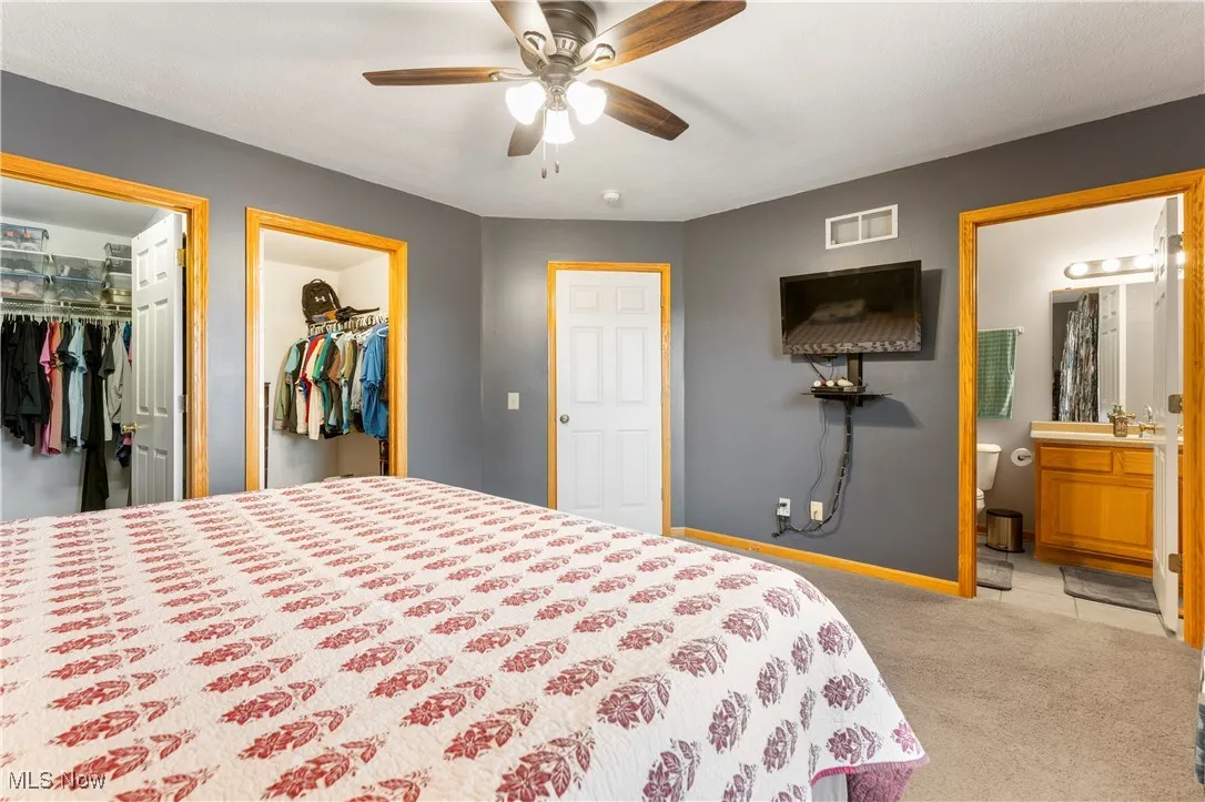 Bedroom with ensuite bathroom, light carpet, and ceiling fan