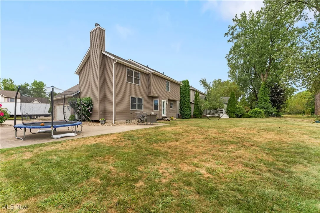 Rear view of property with a trampoline, a patio, a chimney, and a lawn
