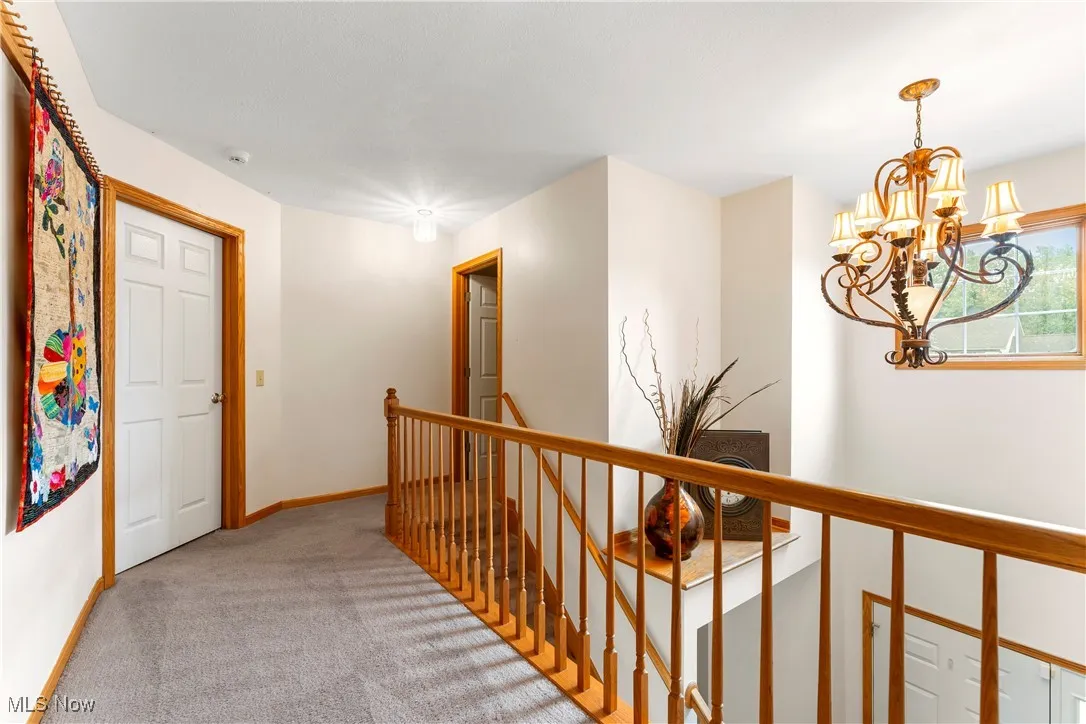 Corridor featuring an upstairs landing, light colored carpet, and a chandelier