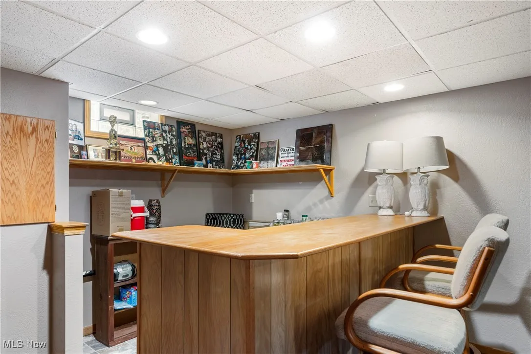 Indoor dry bar featuring a paneled ceiling, open shelves, wooden counters, and a textured wall