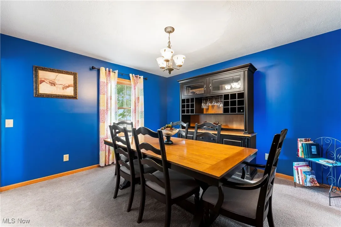 Carpeted dining space featuring baseboards and a chandelier