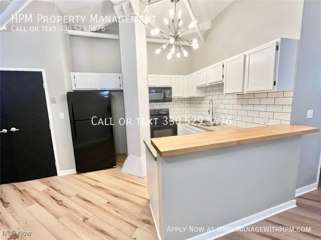 Kitchen with decorative backsplash, a peninsula, black appliances, a high ceiling, and butcher block countertops