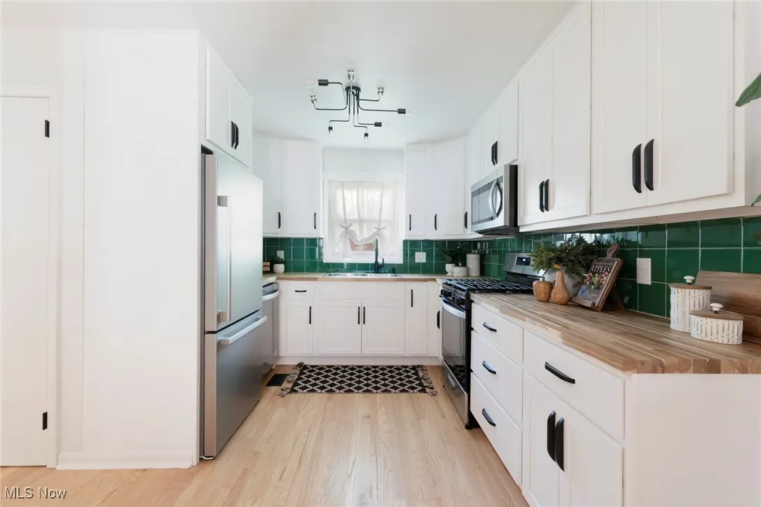 Kitchen with white cabinetry, stainless steel appliances, light wood finished floors, and tasteful backsplash