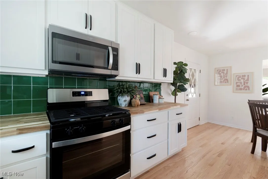 Kitchen with butcher block countertops, appliances with stainless steel finishes, white cabinetry, decorative backsplash, and light wood finished floors
