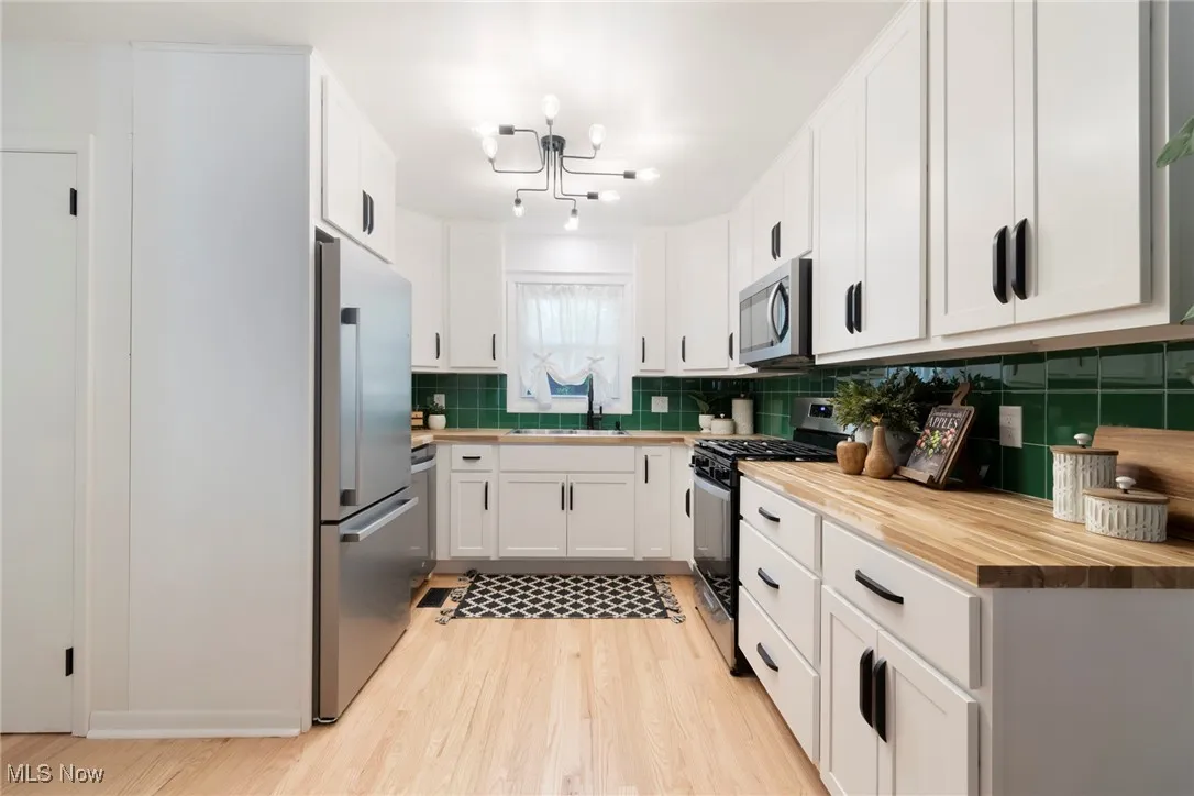 Kitchen with butcher block counters, light wood-type flooring, white cabinets, appliances with stainless steel finishes, and backsplash