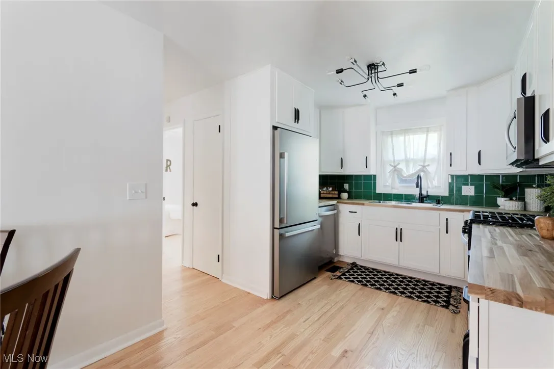 Kitchen with stainless steel appliances, decorative backsplash, light wood finished floors, and white cabinets