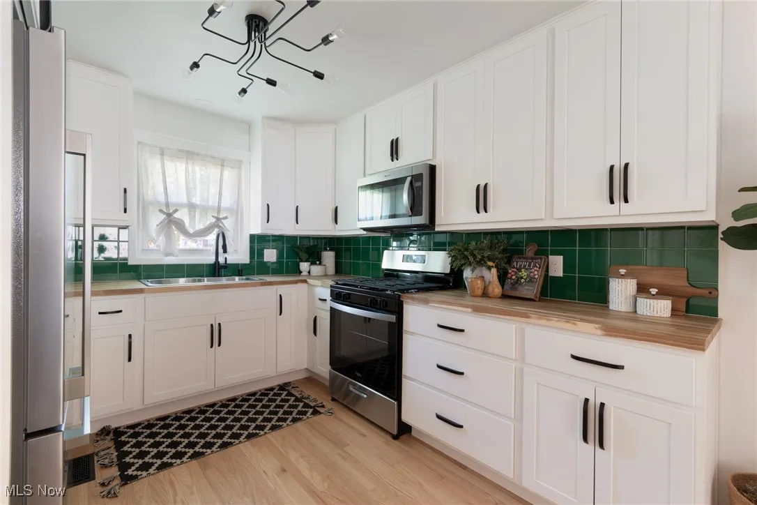 Kitchen featuring white cabinets, appliances with stainless steel finishes, light wood finished floors, and butcher block countertops