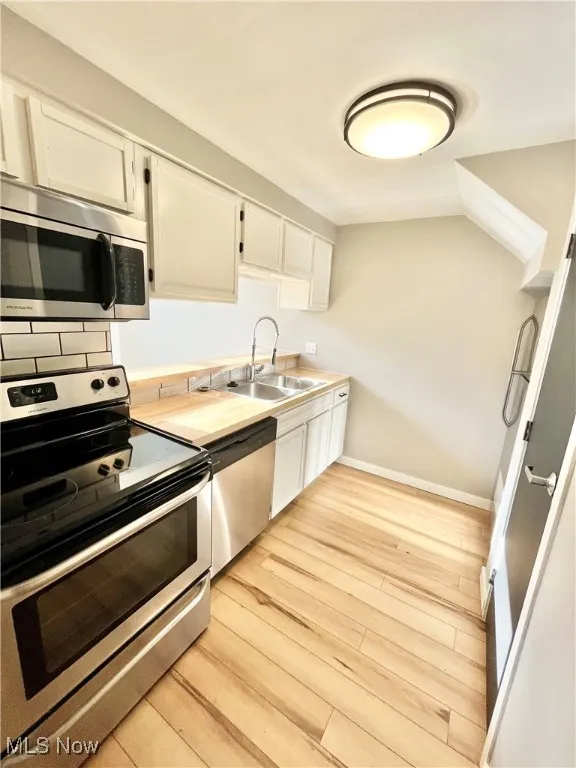 Kitchen featuring stainless steel appliances, white cabinetry, light wood-style flooring, and light countertops
