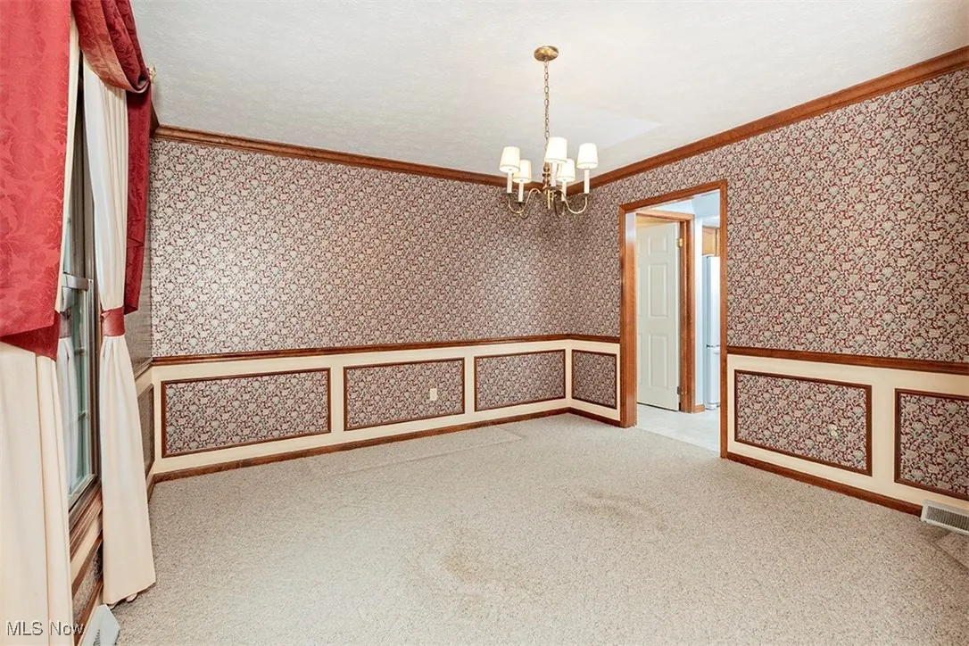 Spare room with crown molding, carpet flooring, wallpapered walls, a chandelier, and a textured ceiling