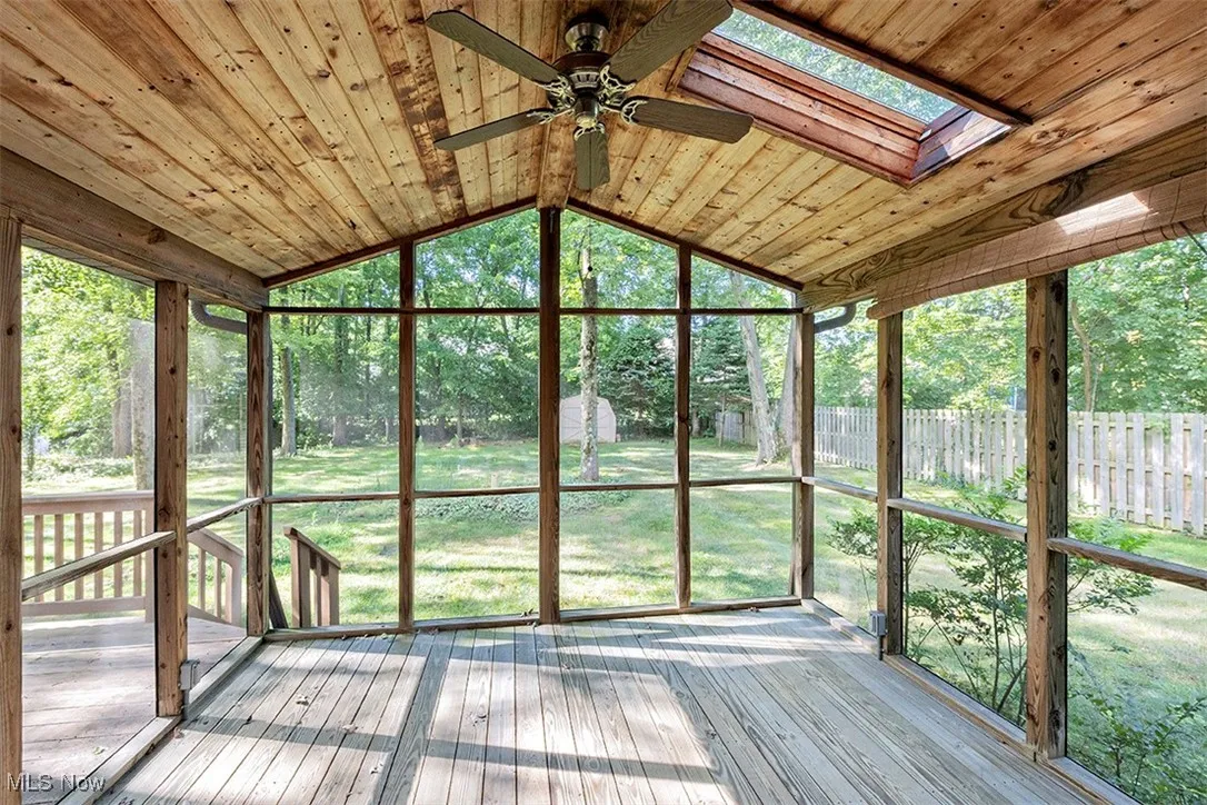 Unfurnished sunroom featuring vaulted ceiling, ceiling fan, a wooden deck, and a skylight